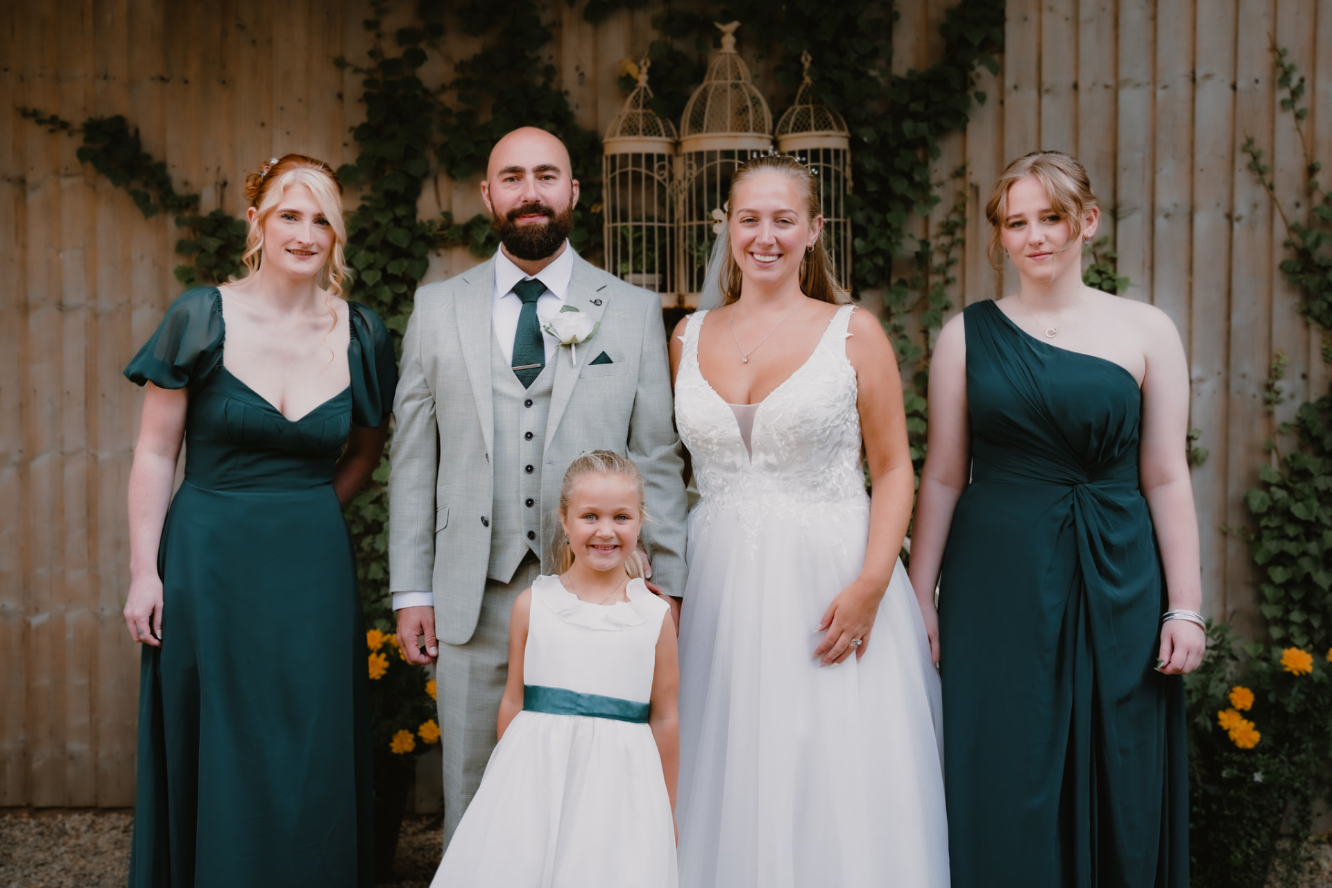 Newlyweds with their wedding party in emerald gowns before an ivy-clad wall