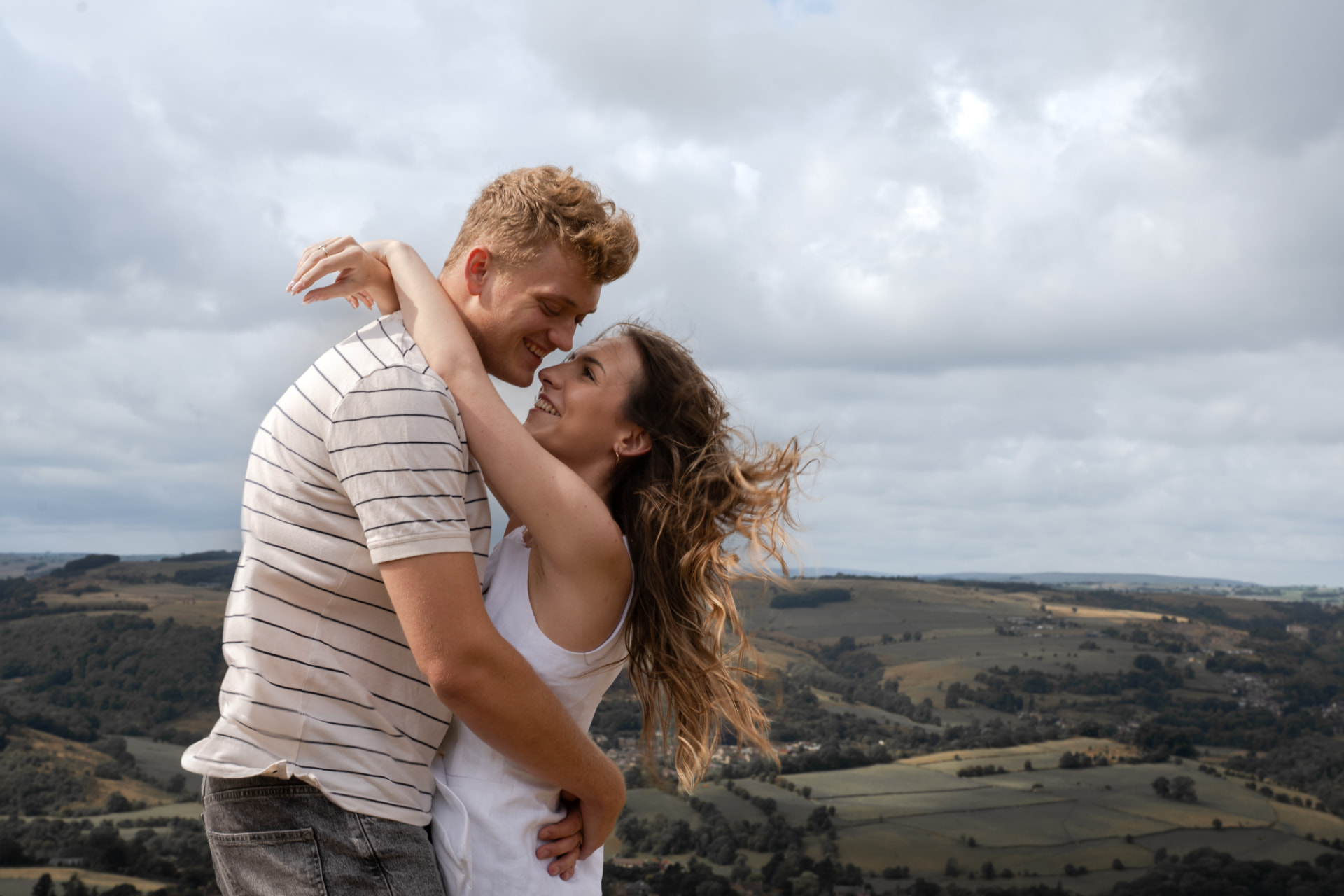Engaged couple embracing on a windswept hill above the South Yorkshire valleys